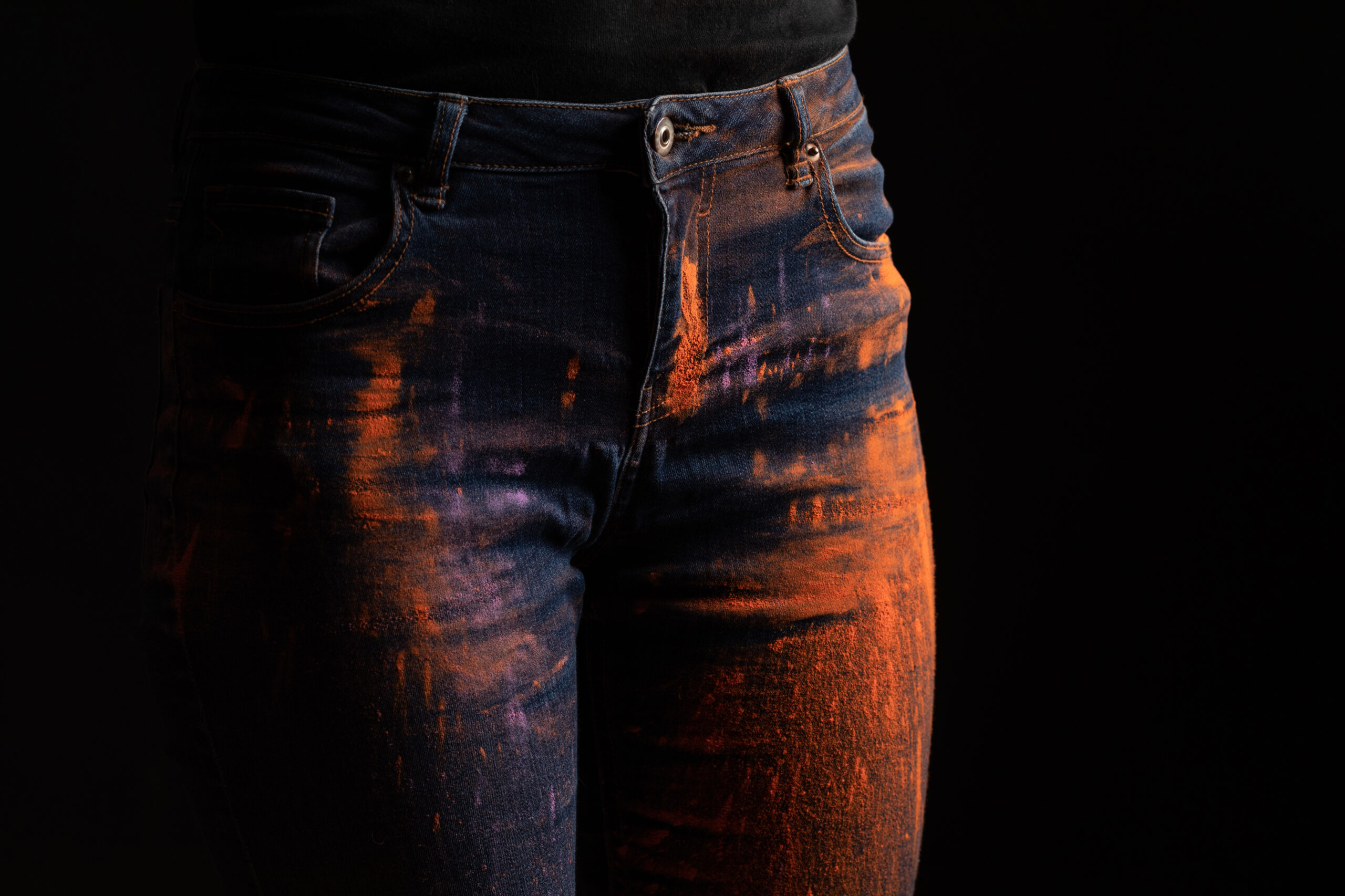 cropped view of woman with orange colorful holi paint powder on jeans isolated on black