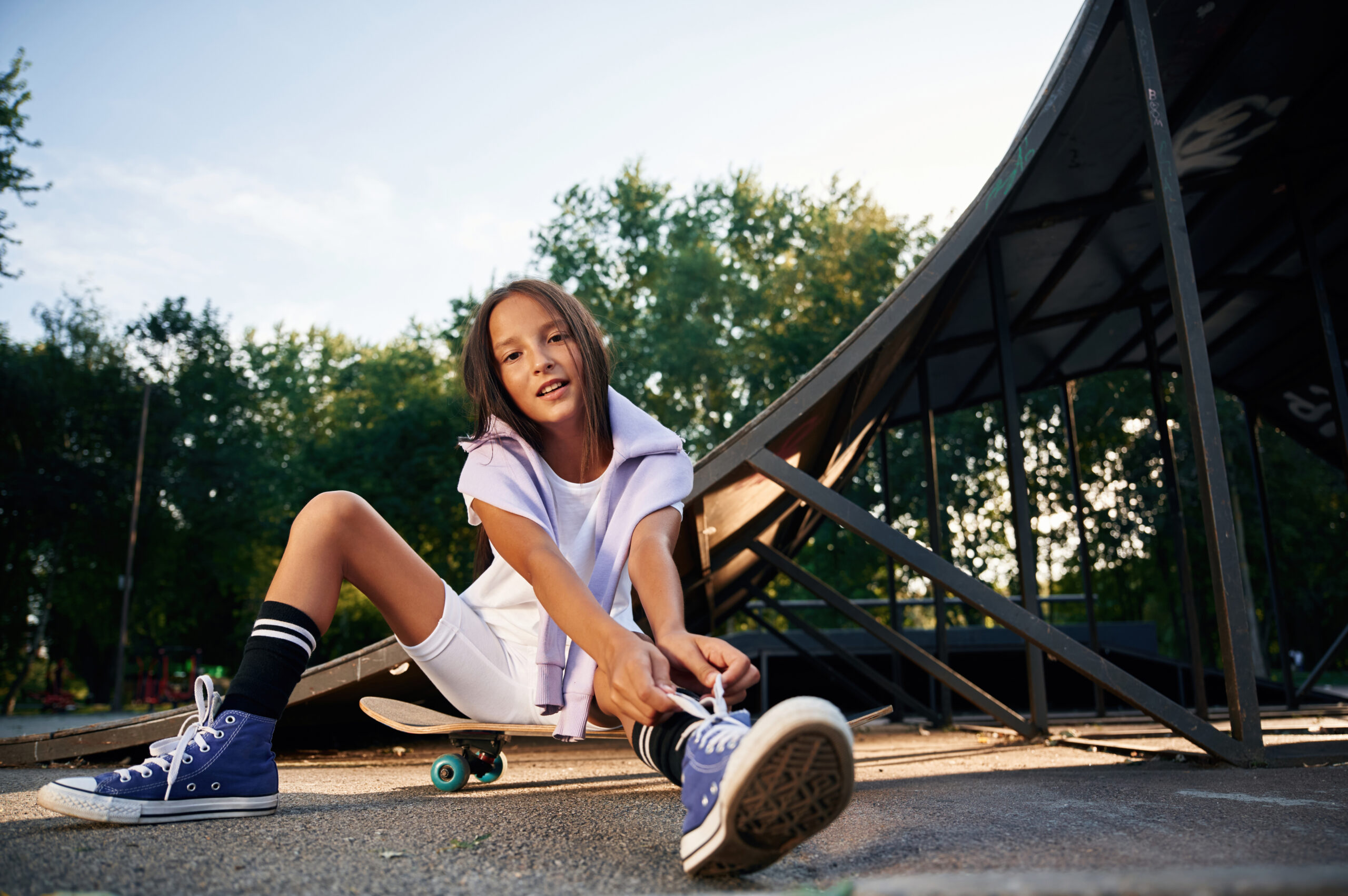 Beautiful summer time in the park, sitting. Happy little girl with skateboard outdoors