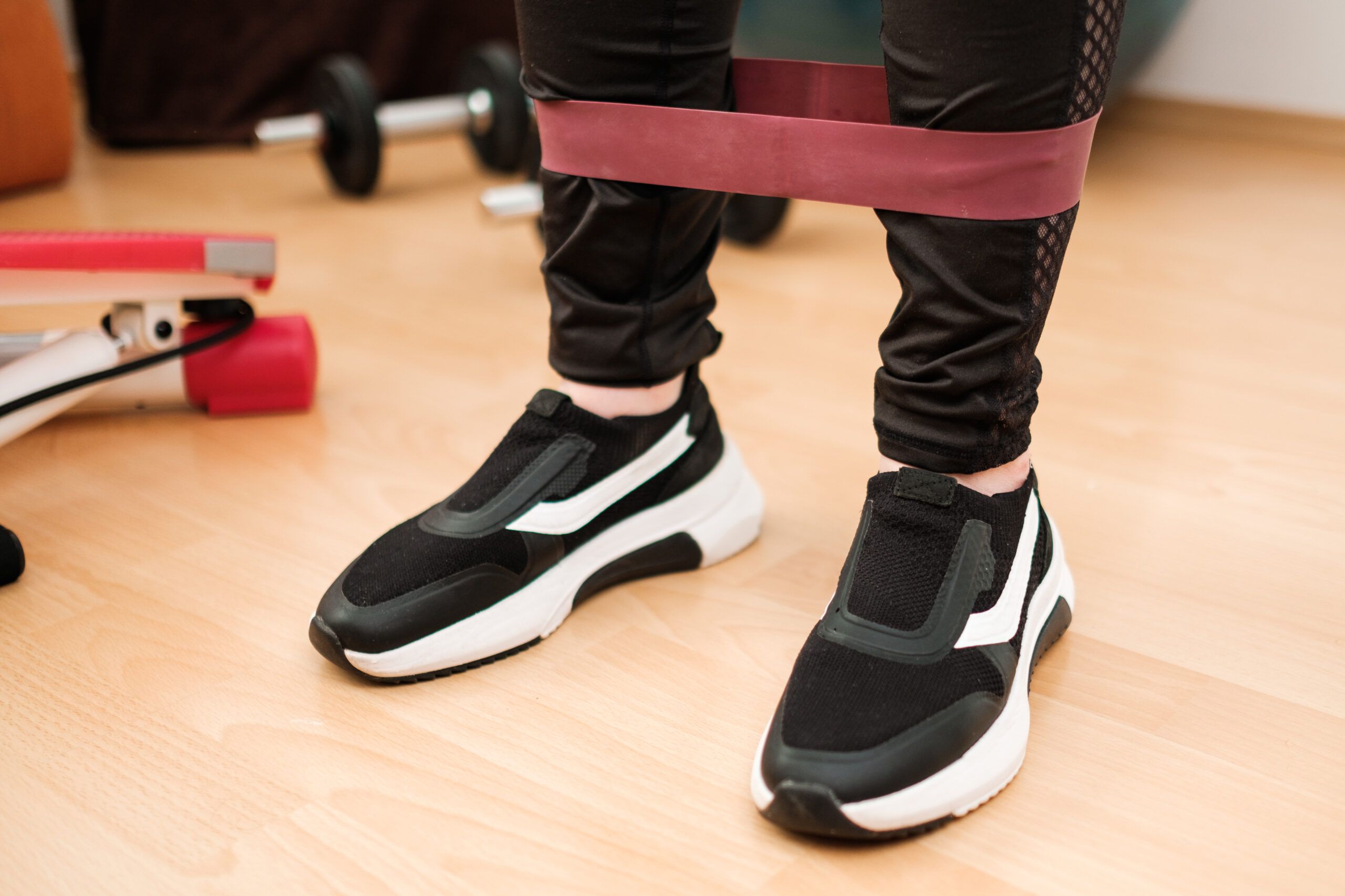 Female legs in sports leggings and sneakers doing exercises with fitness elastic bands at home during lockdown. Home workout. with resistances bands.