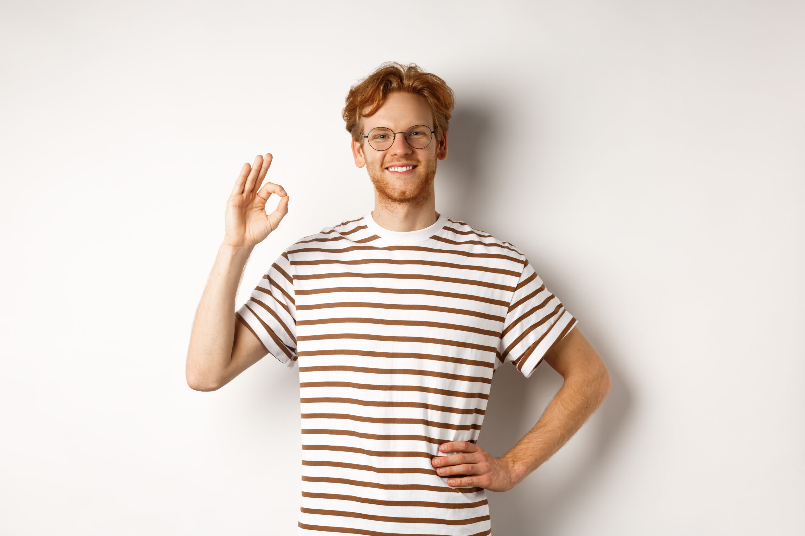 Confident smiling man with red hair assuring you, showing OK sign, guarantee quality, recommending something good, standing over white background